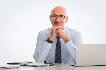Fototapeta premium Mid aged businessman sitting at desk and using notebook for work against isolated white background