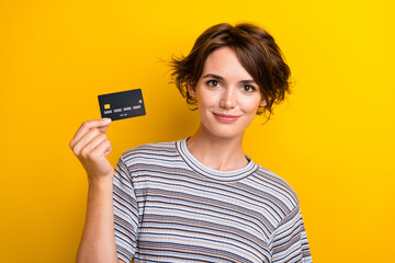 Portrait of satisfied intelligent adorable girl wear grey t-shirt demonstrate plastic card in hand isolated on yellow color background