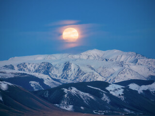 Big moon over a snowy mountain. Night replaces the full moon day.