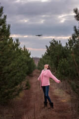 Naklejka na ściany i meble Young woman in knitted pink in countryside among coniferous trees in forest posing for drone camera