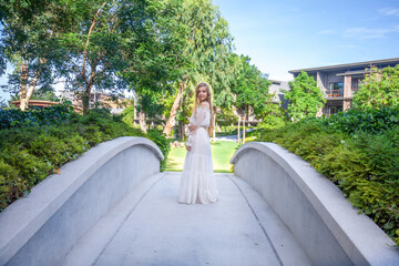 Young woman in elegant white dress strolls through a lush, tropical resort. Graceful female traveler, dressed in white, explores a modern hotel surrounded by greenery. Thailand vacation bliss. - Powered by Adobe