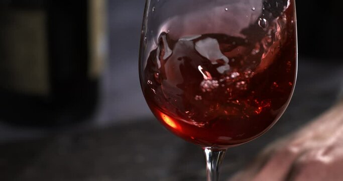 Super slow motion macro of fine quality red wine poured in transparent glass is being checked of quality by male winemaker or sommelier in wine cellar.
