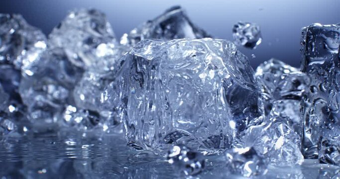 Super slow motion top view close up of ice cool cubes are falling with splashing water drops in transparent clear glass with pure fresh crystal liquid isolated on  frozen background