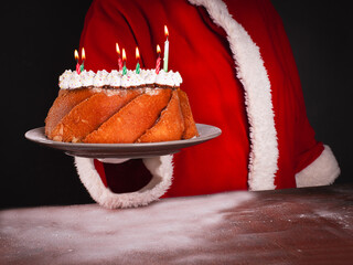 Santa Claus serving cake with candles Cooking, holiday food concept.