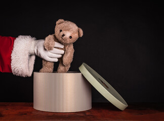Santa Claus takes out a cute teddy bear from a gift box.