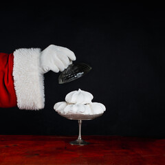 Santa Claus treats you to meringue, a sweet treat. Celebrate Christmas. Black background with copy space.