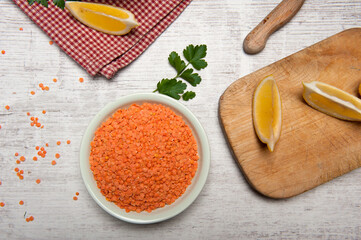 Top view of a bowl of red lentils, onion, garlic  and lemons quarters  on a white vintage wooden table