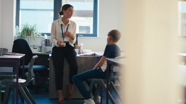 Camera Tracks Across Shot Of Female Secondary Or High School Teacher Sitting In Classroom With Unhappy Male Student After Lesson - Shot In Slow Motion