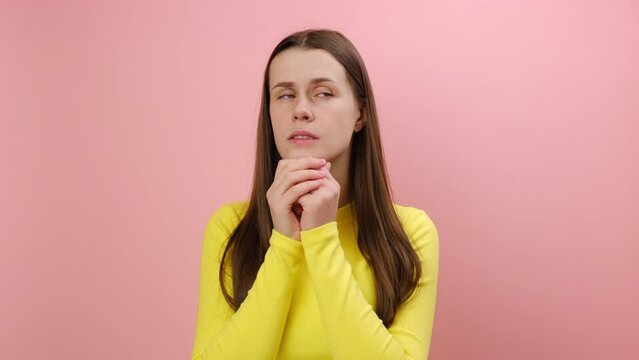 Portrait of panicking young woman biting nails, being nervous terrified, feeling frightened, wearing yellow sweater, posing isolated on pink color background wall in studio. Anxiety disorder concept