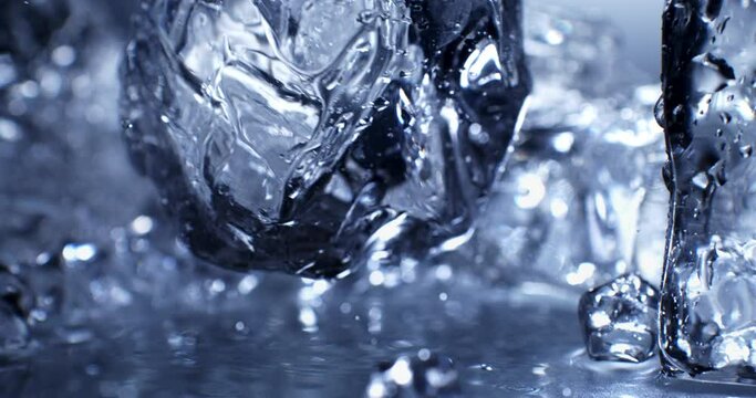 Super slow motion top view close up of ice cool cubes are falling with splashing water drops in transparent clear glass with pure fresh crystal liquid isolated on  frozen background