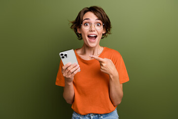 Photo of impressed crazy girl dressed orange t-shirt hold smartphone arm on head astonished staring isolated on khaki color background