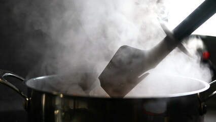 Smoke coming out from cooking food pan, stirring and preparing meal