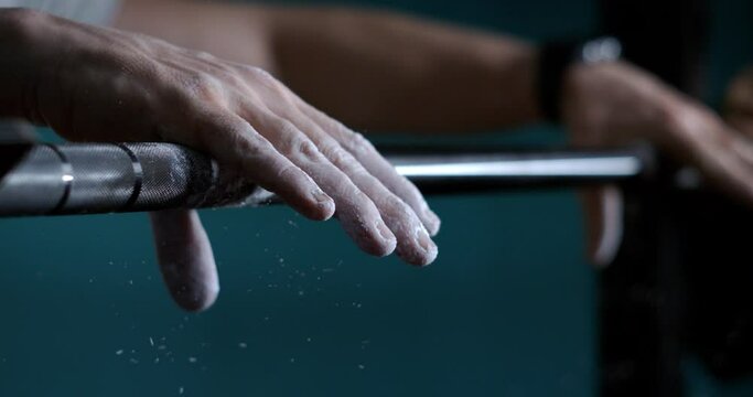 Super slow motion macro of male athlete hands with talc is doing workout by lifting weights of barbell row to maintain healthy lifestyle and bodybuilding goals in a gym.