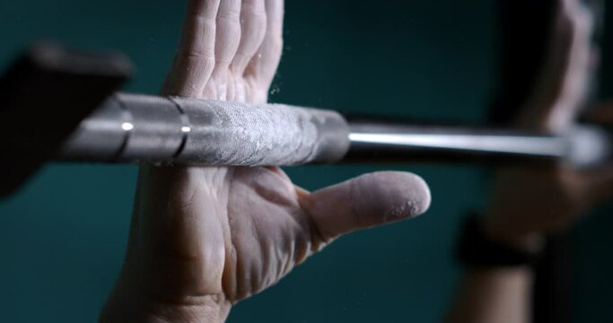 Super slow motion macro of male athlete hands with talc is doing workout by lifting weights of barbell row to maintain healthy lifestyle and bodybuilding goals in a gym.