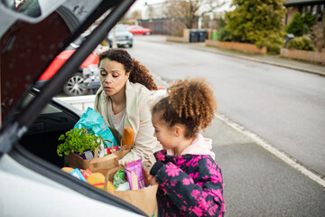 Mother and daughter taking groceries out of car in home driveway