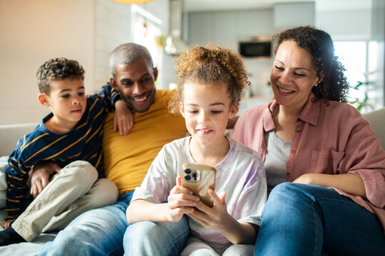 Young mixed family taking a selfie on a smartphone together on the couch at home - Powered by Adobe