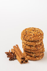 Oatmeal whole grain cookies with cereals isolated on white background. Stack of biscuits with seeds, cinnamon sticks and star anise, close up