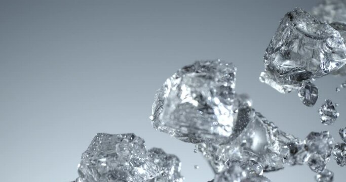 Super slow motion top view close up of ice cool cubes are falling with splashing water drops in transparent clear glass with pure fresh crystal liquid isolated on frozen background