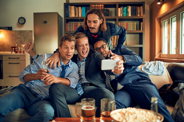 Group of friends taking selfie, happy men enjoying party at home, multiethnic males with drinks,...