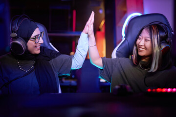 Side view portrait of two young women playing video games together and high five celebrating...