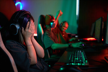 Side view portrait of female gamer hiding face in hands devastated by defeat in cybersports club, copy space