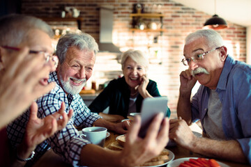 Senior people laughing at smartphone in home kitchen