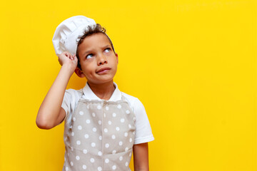 pensive african american boy in uniform and chef's hat plans and thinks on yellow isolated...