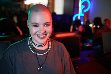 Portrait of bald young woman smiling at camera in cybersport club interior, copy space