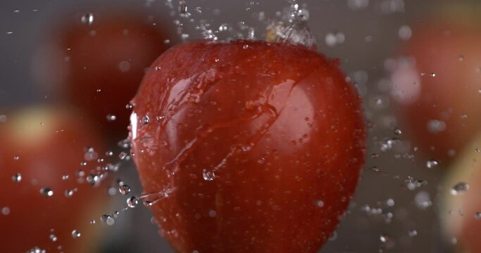 Super slow motion macro of splashing clear pure water drops are falling on spinning fresh ripe bio organic red apple fruit isolated on soft warm background. 