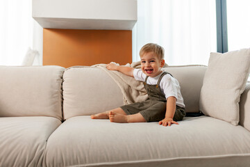 little boy 2 years old sits on soft comfortable sofa at home and laughs, happy child smiles