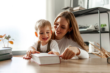 young mother with her little son reading book, 2-year-old boy learning to read with his parent, woman teaching