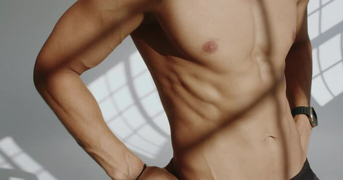 Cropped view on shirtless man with muscular body after workout. Sporty handsome male bodybuilder with athletic shape. Fitness model with naked torso in studio