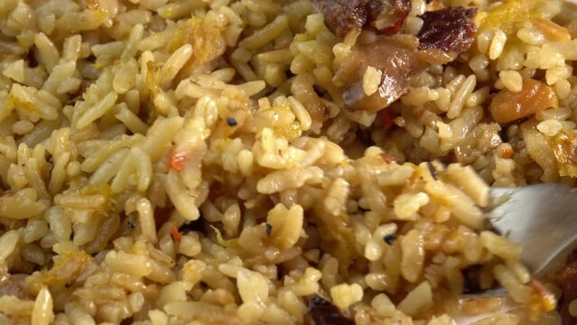 Fork scoops uzbek pilaf with meat side view closeup. Traditional East Asian dish with chickpeas, barberries, cumin, long grain rice and lamb