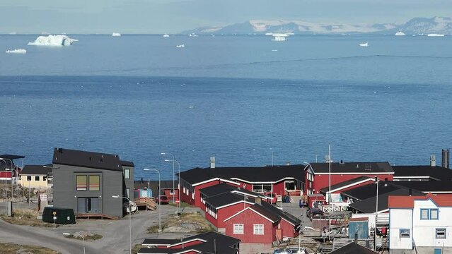 Ocean, icebergs and Greenland settlement. Greenland arctic village Ilulissat. Colorful inuit houses. Greenland polar landscape. Travel to the Arctic Circle. Climate change, global warming.