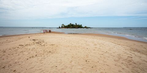 Pessoas distantes caminhando na areia da praia em direção a uma ilha no nordeste brasileiro