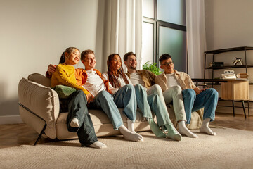 multiracial group of young friends sitting on sofa at home hugging and looking at camera