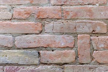 Ancient rough red brick wall with cracks and holes, close-up. Background texture