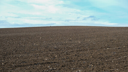 Ploughed farm field under a clear cloudy blue sky in an agricultural landscape. Open space area.
