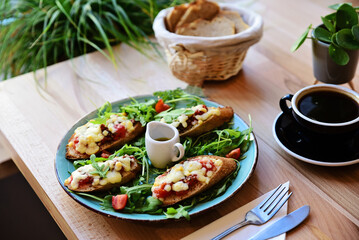 Fresh breakfast on a plate with black cup of coffee on a table in restaurant. Delicious bruschetta with cheese and greens for lunch. Close up.