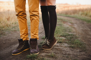 Photo of a couple's legs, the man is wearing orange pants, behind him is his wife standing on her tiptoes and reaching for him, a romantic photo