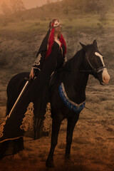 A warrior girl in a black oriental costume on a black horse with a katana in her hands.
