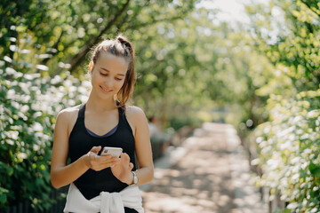 Active woman using smartphone on a nature trail, sunny day.