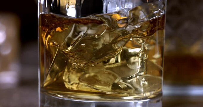 Super Slow Motion Detail Shot of Pouring old malt burbon Whiskey on Ice Cubes into pure Glass at 1000fps.