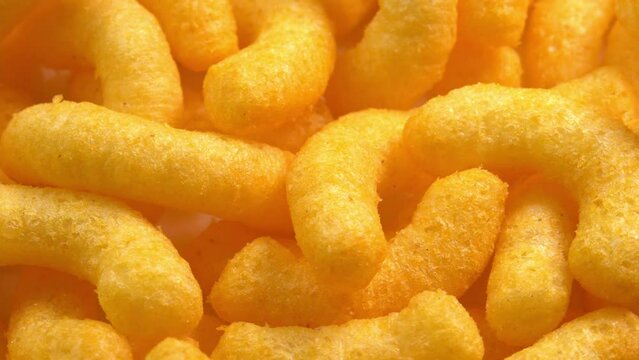 Cheesy corn sticks rotates closeup side light. Crispy cheese snack. Crispy fluffy corn chips for breakfast
