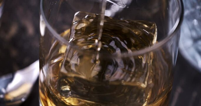 Super Slow Motion Detail Shot of Pouring old malt burbon Whiskey on Ice Cubes into pure Glass at 1000fps.
