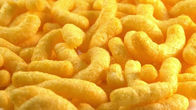Cheesy corn chips rotates on plate side light. Crispy cheese snack. Crispy fluffy corn sticks for breakfast