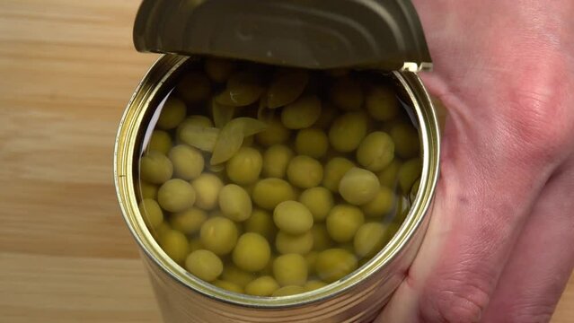 Hands opening tin can with green peas kernels ready to eat meal close-up. Showing how to open a can with pull tab. Non perishable food storage products in the home kitchen