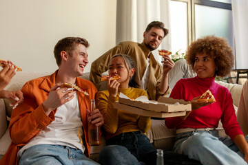 multiracial group of young people at house party eating pizza and drinking beer and having fun with...