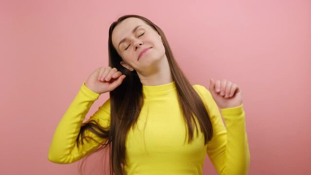 Portrait of sleepless young caucasian woman yawning and raising hands up, feeling fatigued, wakes up early in morning, wearing yellow sweater, posing isolated over pink color background wall in studio