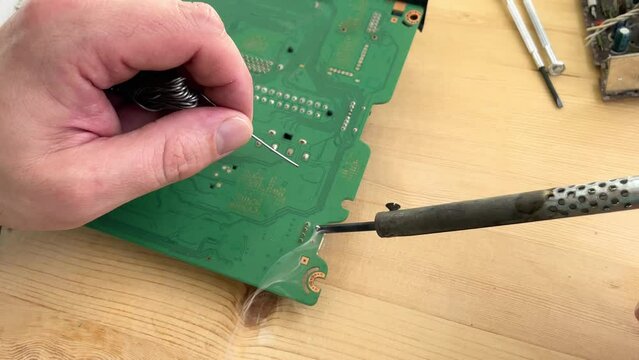 Soldering a micro chip processor with iron tool on a green circuit boad. Electroncs service technology and macro computer concept background.